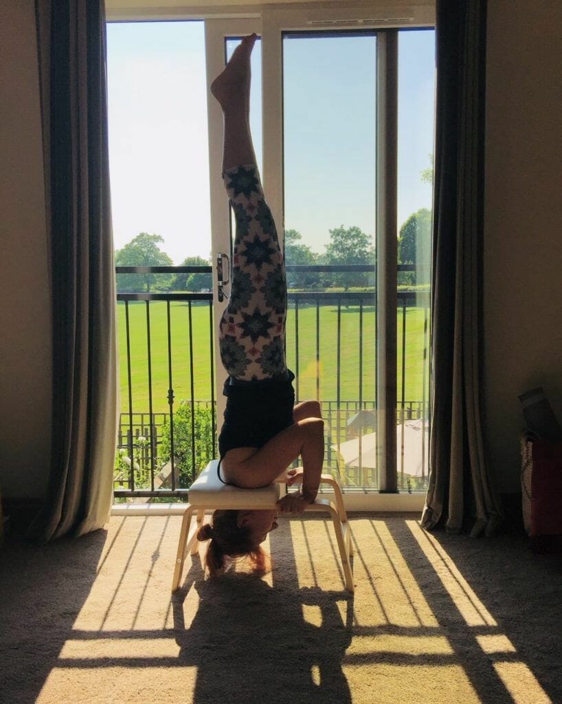 a person doing a handstand on a chair in front of a window.
