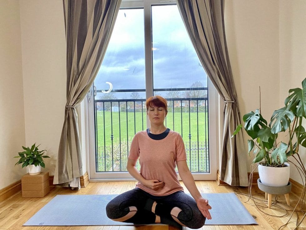 a woman sitting on a yoga mat in front of a window.
