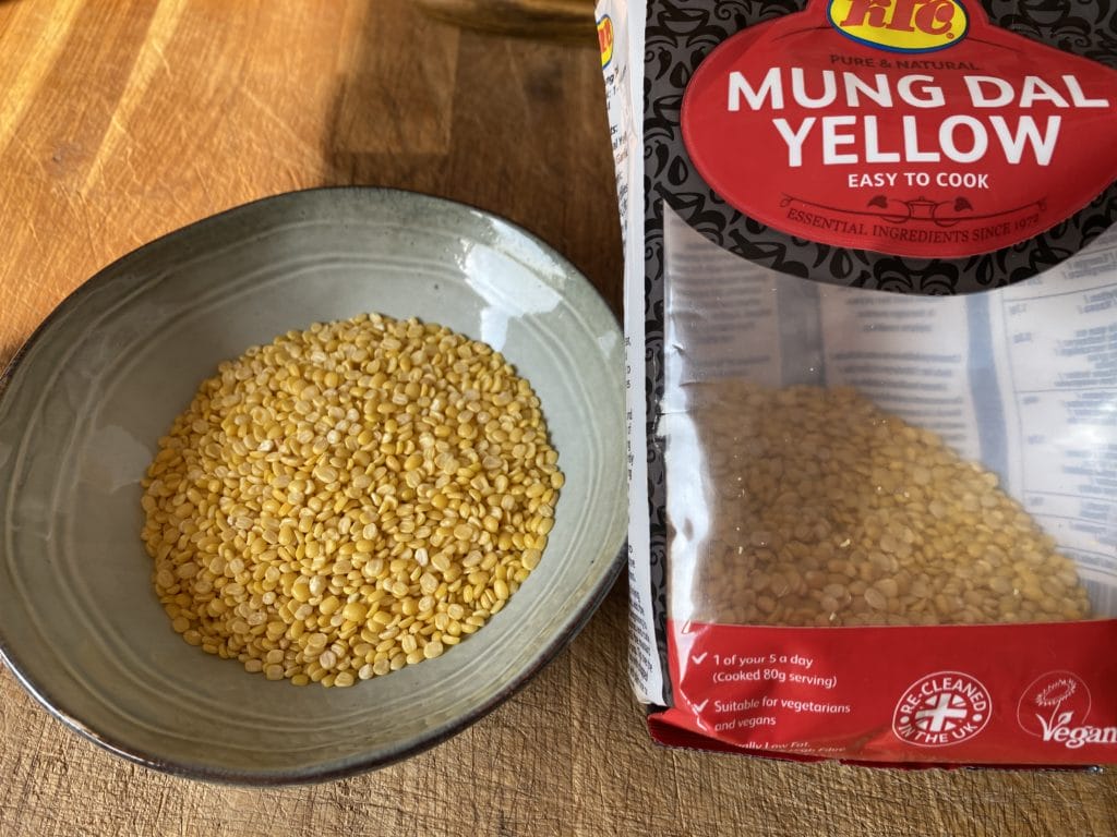 a bag of mung dal yellow next to a bowl of rice.