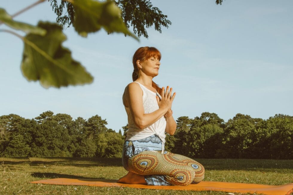a woman sitting on a yoga mat in a park.